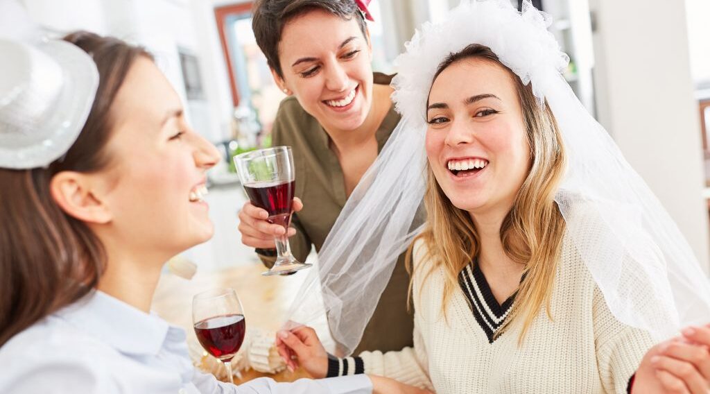 group of women, one with veil in hair and glass of wine in hand